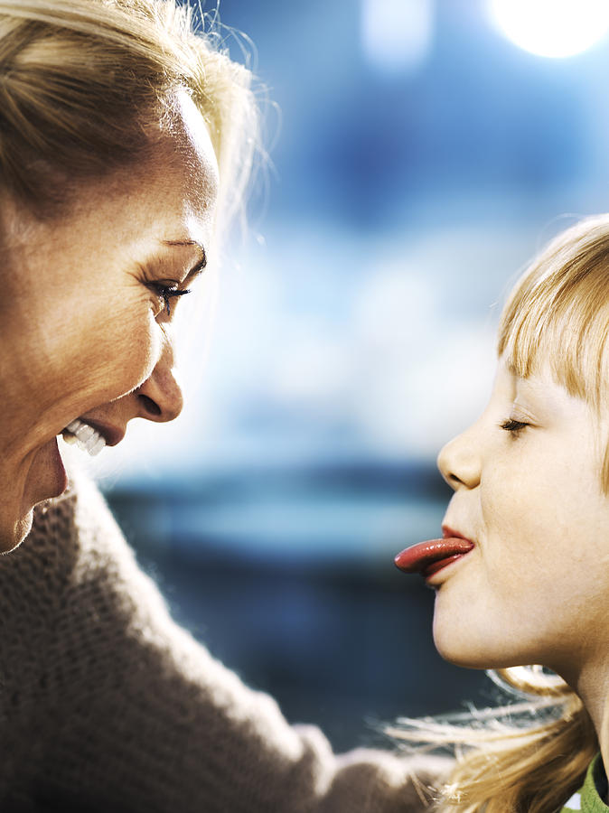 Profiles of mother and daughter (6-7), girl sticking out tongue Photograph by Henrik Sorensen