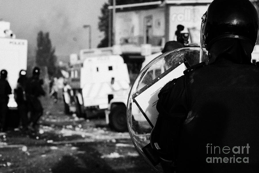 Northern Photograph - PSNI riot officer with baton round warning on shield watches rioting on crumlin road at ardoyne shop by Joe Fox