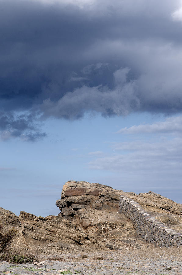 Cala Mesquida stone wall against rocks with a stormy sky above - Putting walls to heaven Photograph by Pedro Cardona Llambias