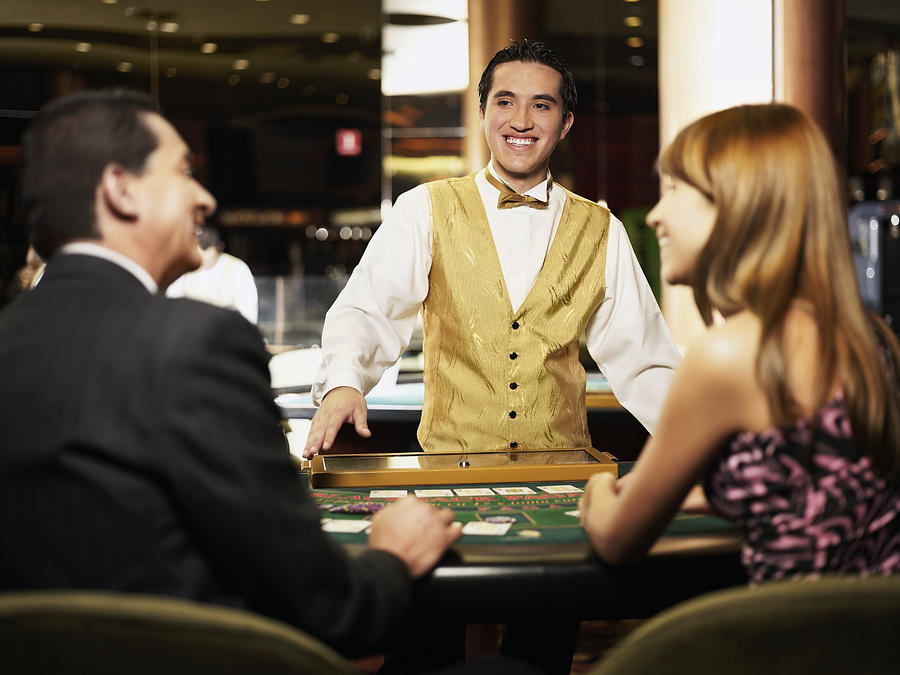 Rear view of a mature man and a young woman sitting at a gambling table with a casino worker smiling in front of them Photograph by Glowimages