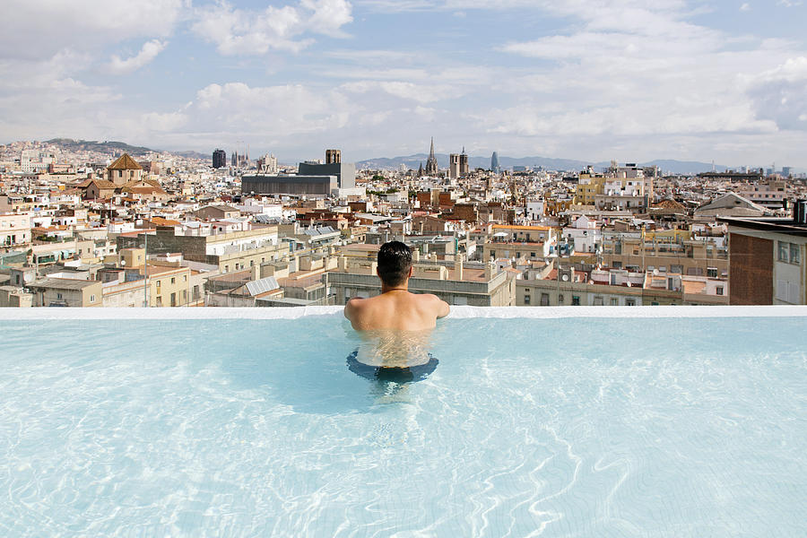 Rear view of a young man relaxing in the pool and looking at Barcelona city skyline Photograph by Alexander Spatari