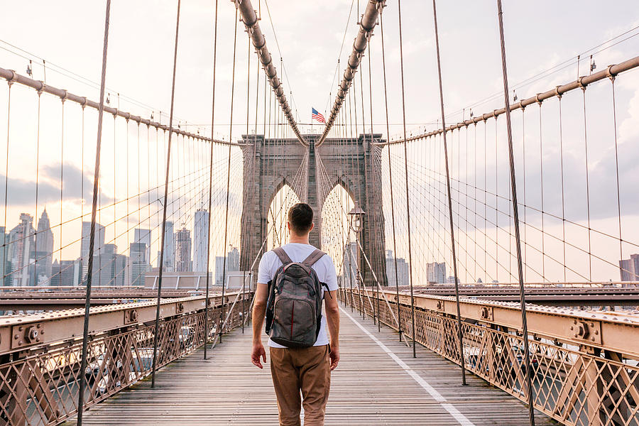 Rear view of a young man with backpack walking on Brooklyn Bridge, New York City, USA Photograph by Alexander Spatari