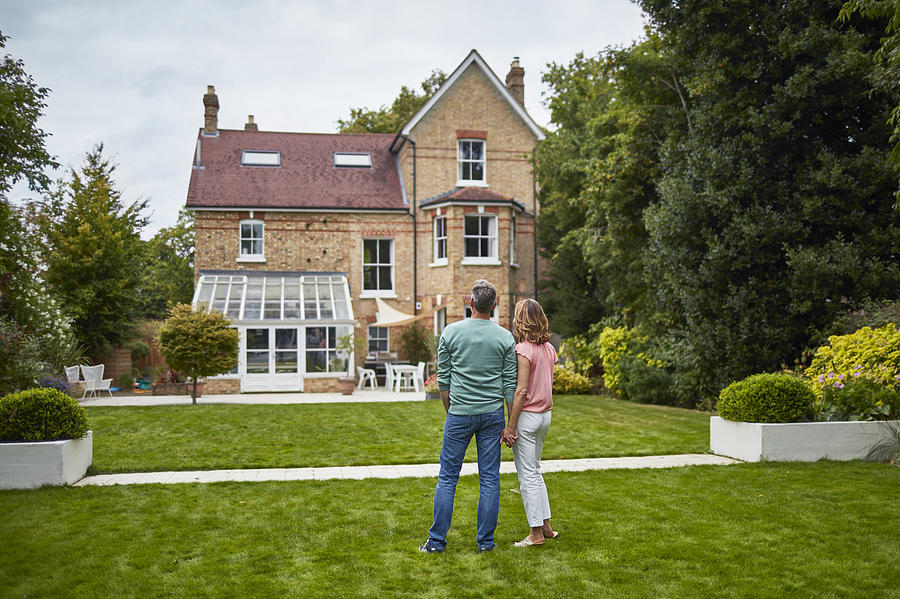 Rear view of couple on grass looking at house Photograph by Xavierarnau