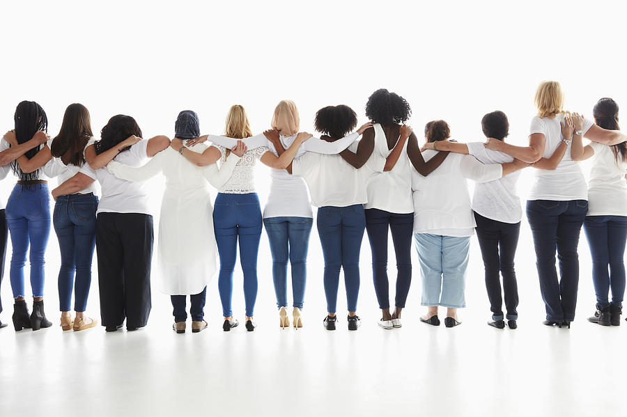 Rear view of diverse women standing in a row hugging Photograph by Colin Anderson Productions Pty Ltd