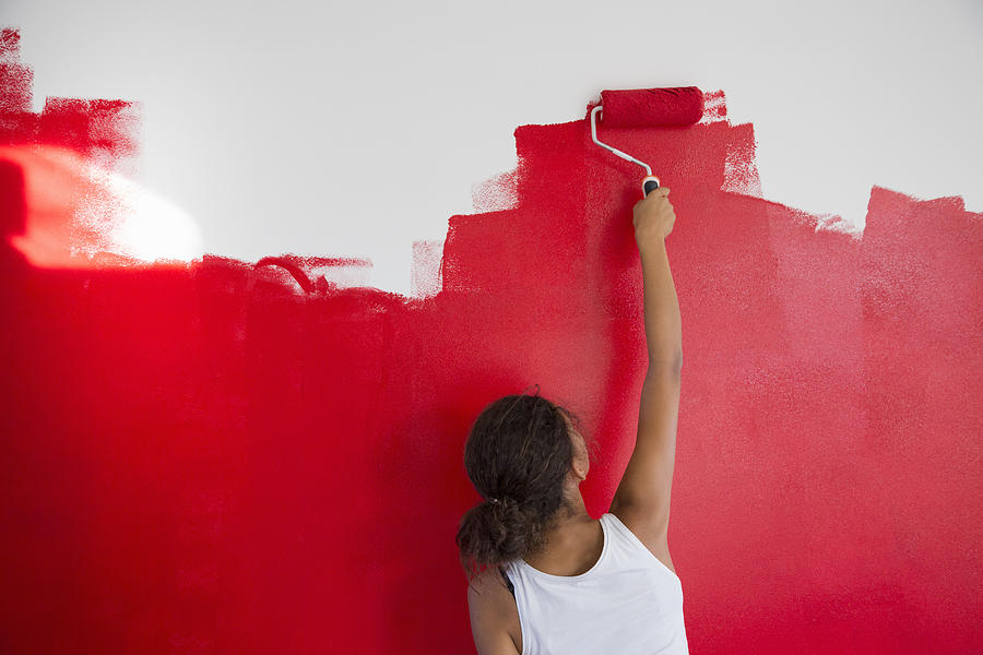 Rear view of girl painting red wall with paint roller Photograph by Easy Production