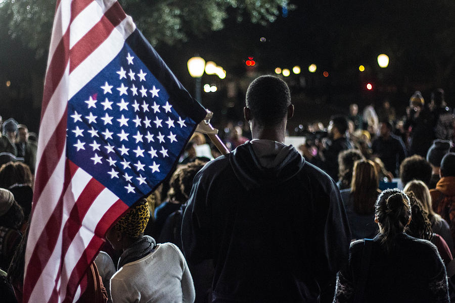 Rear View Of Man Holding American Flag In Crowd Photograph by Joe Ybarra / EyeEm
