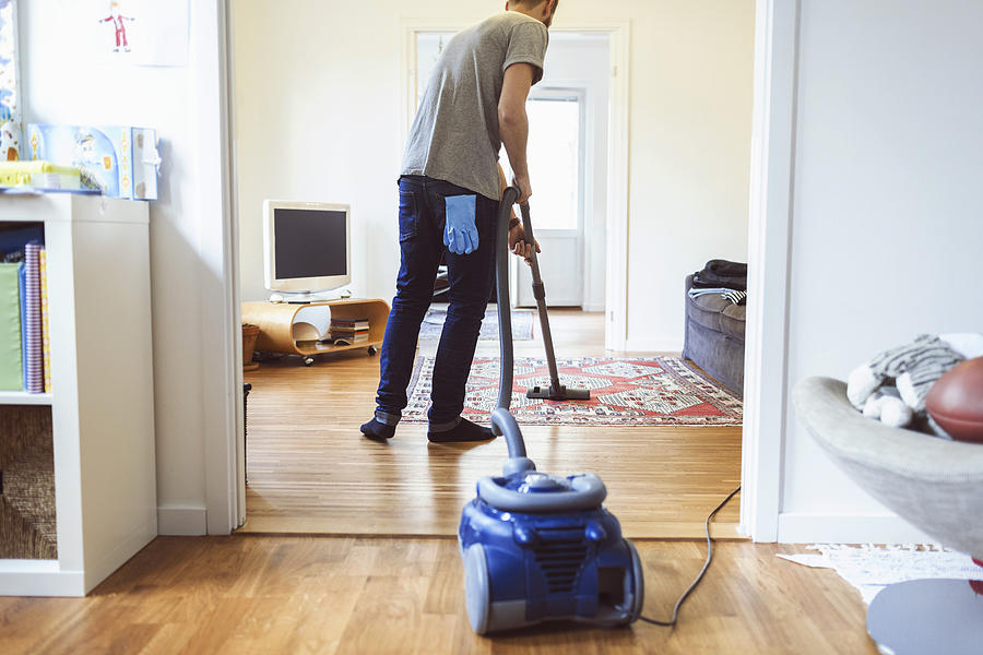 Rear view of man vacuuming carpet Photograph by Maskot