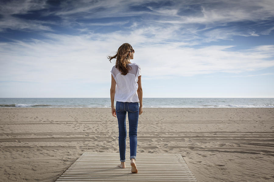 Rear view of mid adult woman strolling on beach, Castelldefels, Catalonia, Spain Photograph by Quim Roser