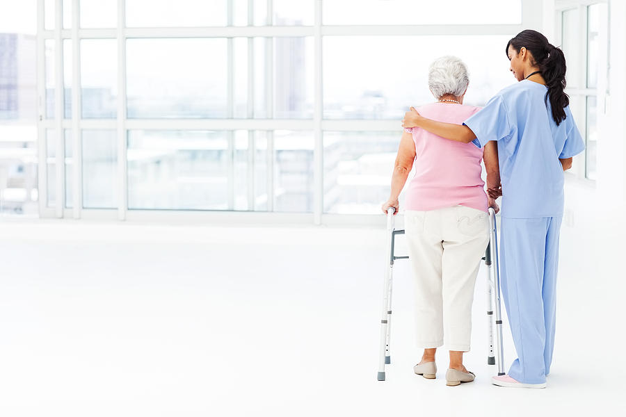 Rear View Of Nurse Assisting Senior Patient With Walker Photograph by Neustockimages