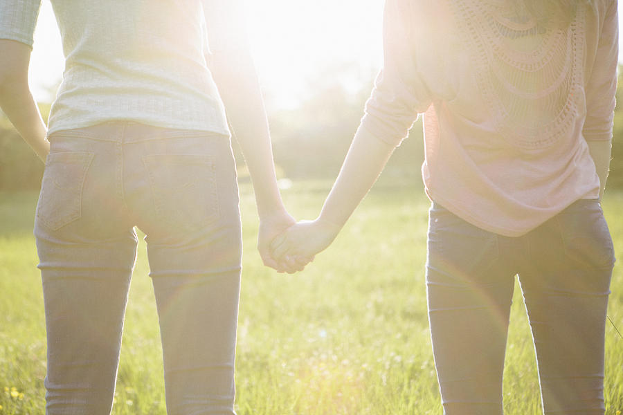Rear View Of Two Young Women Holding Hands, Backlit Photograph by Fotografixx