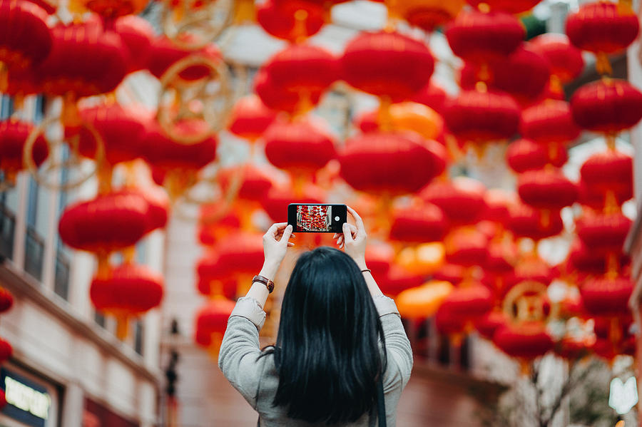 Rear view of woman taking photos of traditional Chinese red lanterns with smartphone on city street Photograph by D3sign