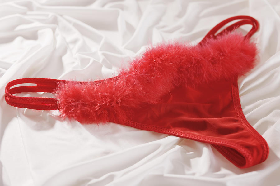 Red ladies underwear with feather detail, against white background Photograph by Martin Harvey