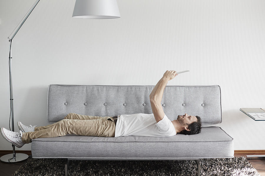 Relaxed man lying on couch holding digital tablet Photograph by Oliver Rossi