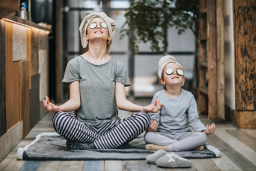 Relaxed mother and daughter exercising Yoga in the morning at home. Photograph by Skynesher