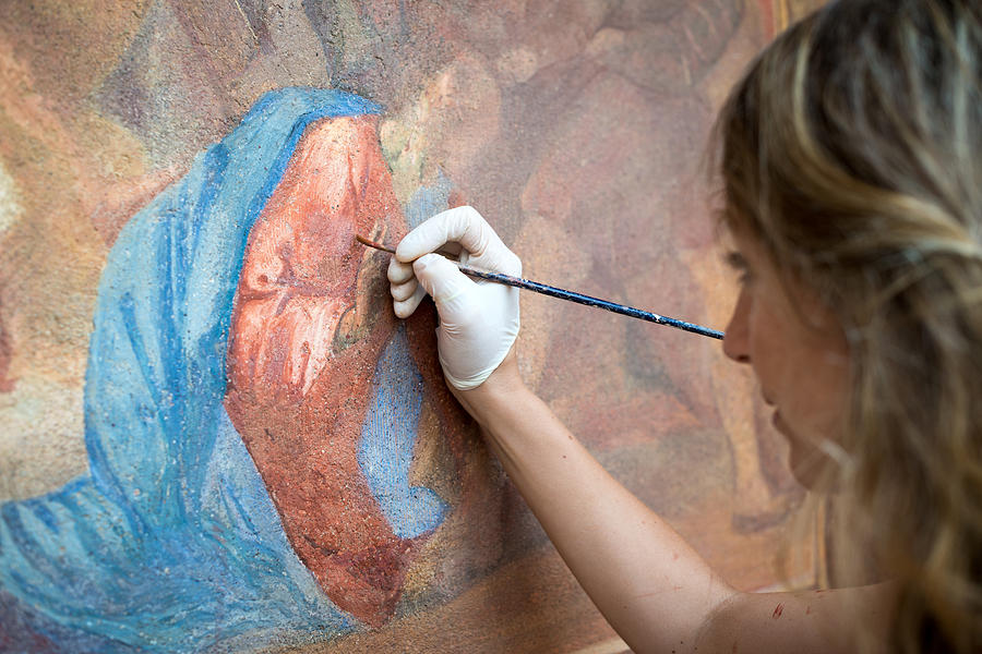 Restorer working on antique outdoor chapel fresco in Italy: Painting restoring of religious art Photograph by Ilbusca