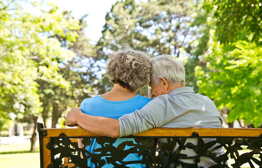 Retired man sitting with arm around woman on bench Photograph by Izusek