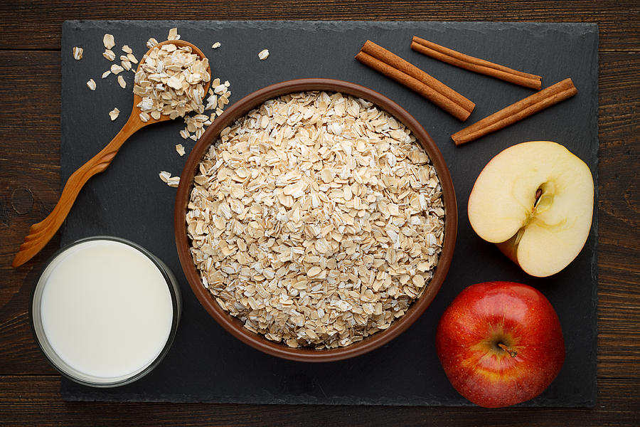 Rolled oat flakes in bowl with apple, cinnamon and milk on slate background. Photograph by Dubravina
