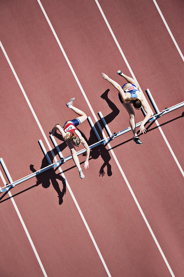 Runners jumping hurdles on track Photograph by Paul Bradbury