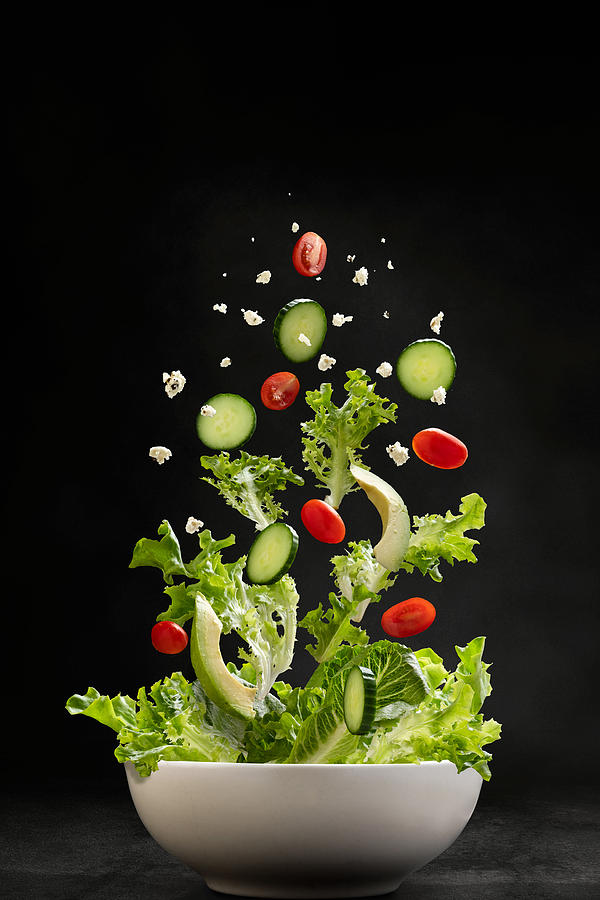 Salad ingredients flying through the air, landing in a bowl Photograph by CarlaMc