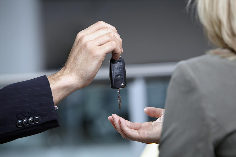 Salesman handing woman car keys in automobile showroom Photograph by Adam Gault