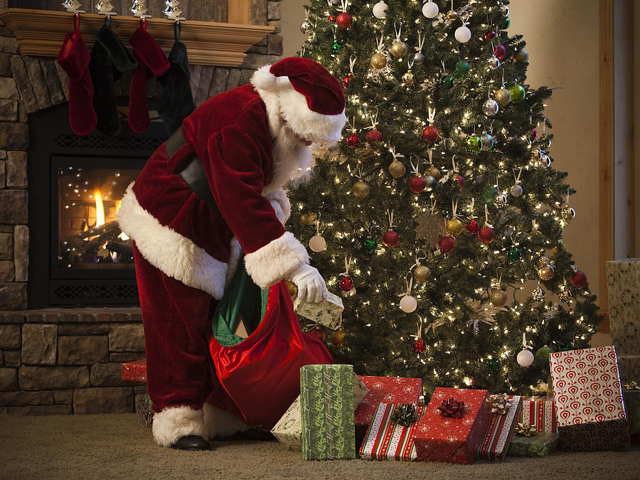Santa Claus Putting Presents Under The Tree Photograph by RubberBall Productions