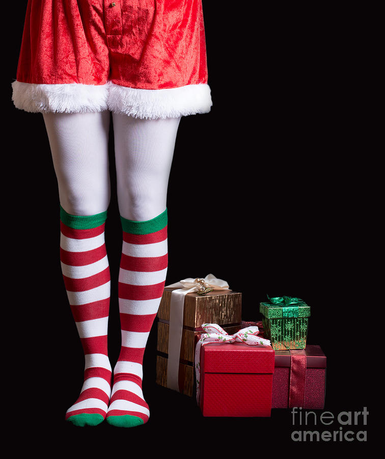 Santas Elf legs next to a pile of Christmas gifts over black Photograph by Edward Fielding