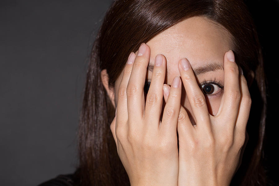 Scared woman peeking through her hands Photograph by Yuichiro Chino