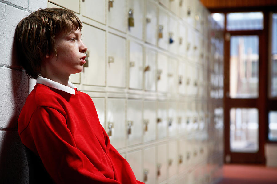 Schoolboy (11-13) sitting in corridor leaning head on wall, side view Photograph by Ableimages