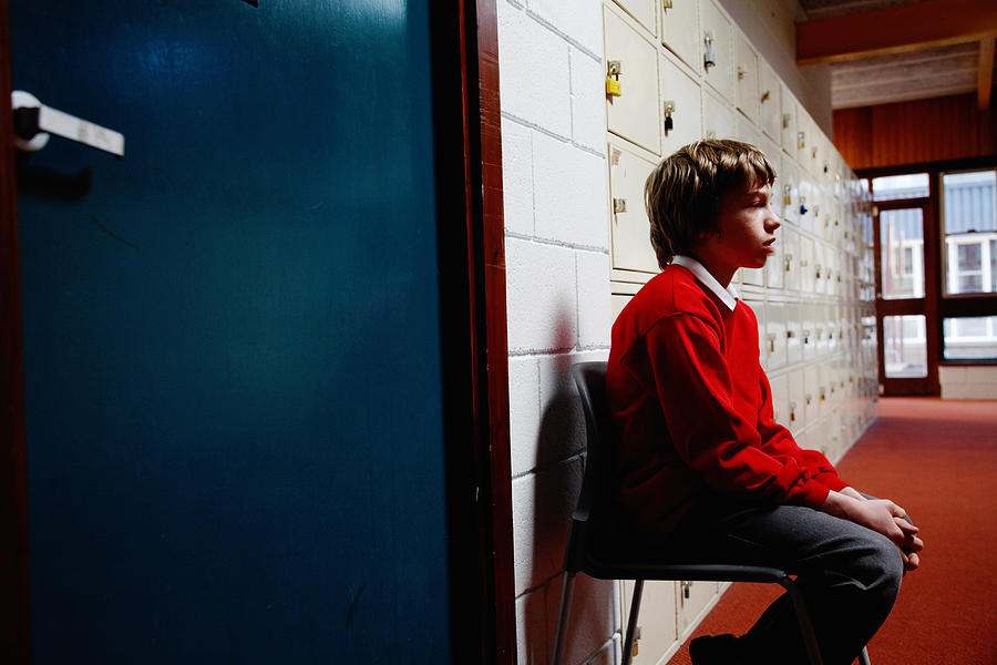 Schoolboy (11-13) sitting on chair in corridor, side view Photograph by Ableimages