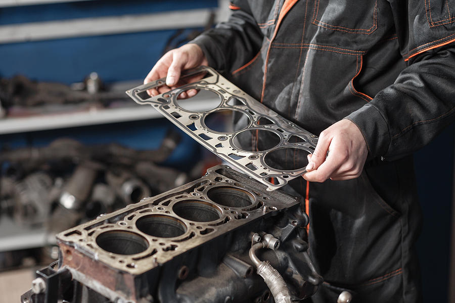 Sealing gasket in hand. The mechanic disassemble block engine vehicle. Engine on a repair stand with piston and connecting rod of automotive technology. Interior of a car repair shop. Photograph by Malkovstock