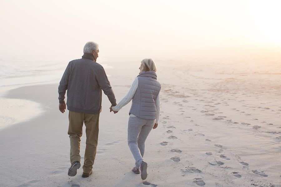 Senior couple walking on a beach together Photograph by Alistair Berg