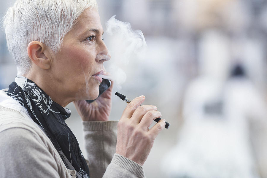 Senior female using electronic cigarette Photograph by Danchooalex