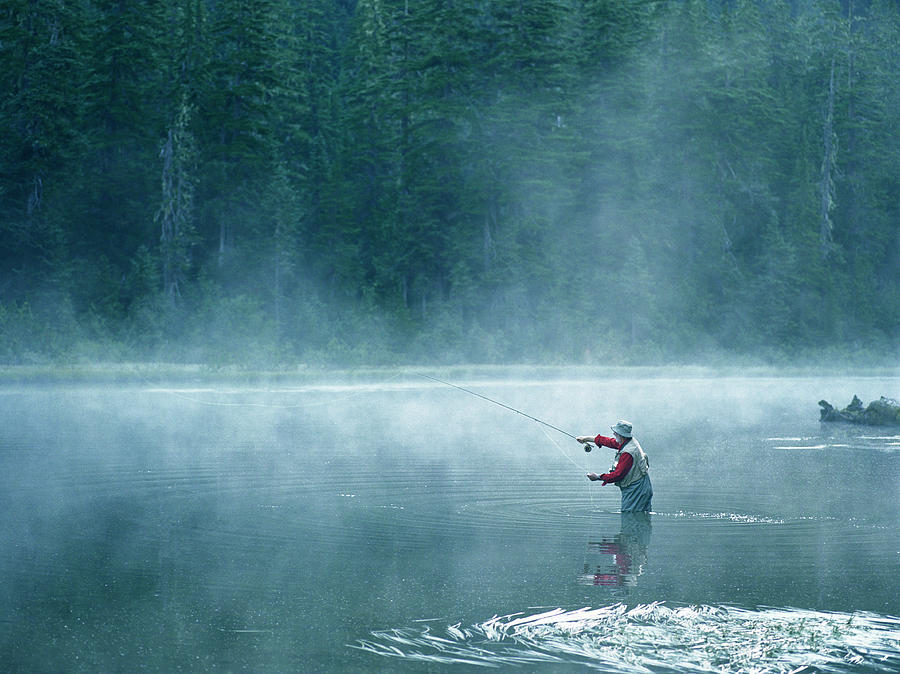 Senior fly fisherman standing in lake covered with fog, casting line Photograph by Mike Powell