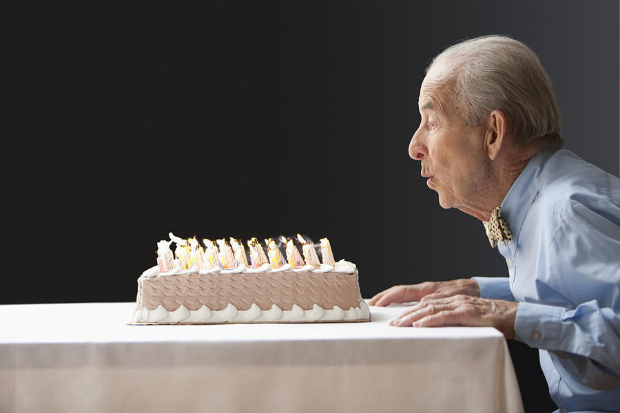 Senior Hispanic man blowing out birthday candles Photograph by Jose Luis Pelaez Inc