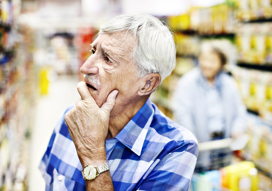 Senior man considers his choice on the supermarket shelf seriously Photograph by RapidEye
