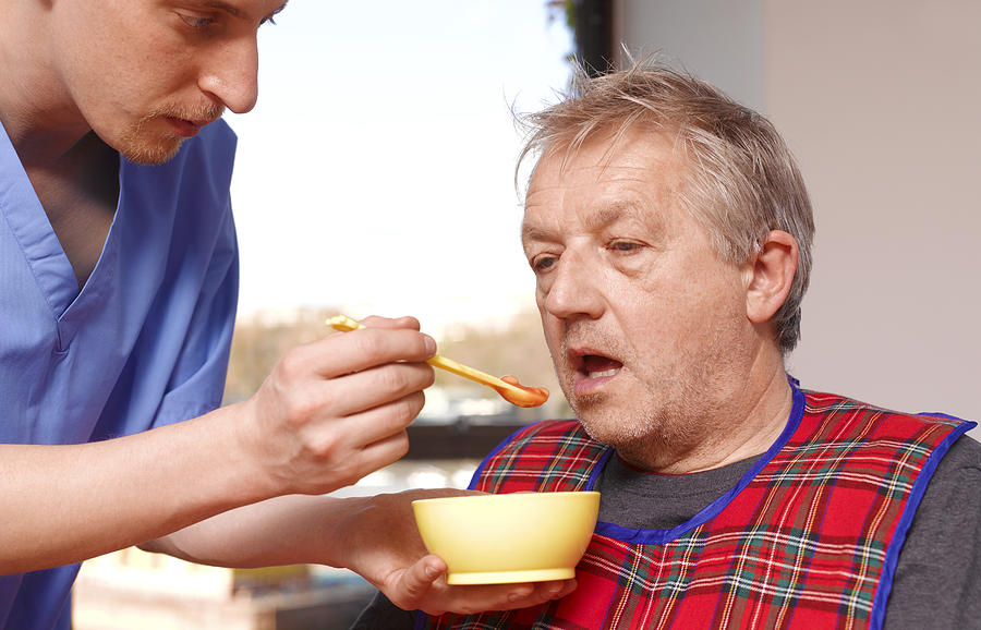 Senior man getting fed by carer in care home Photograph by Peter Dazeley