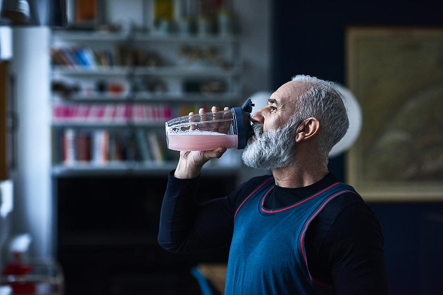 Senior man wearing sports top gulping health drink from container Photograph by 10000 Hours