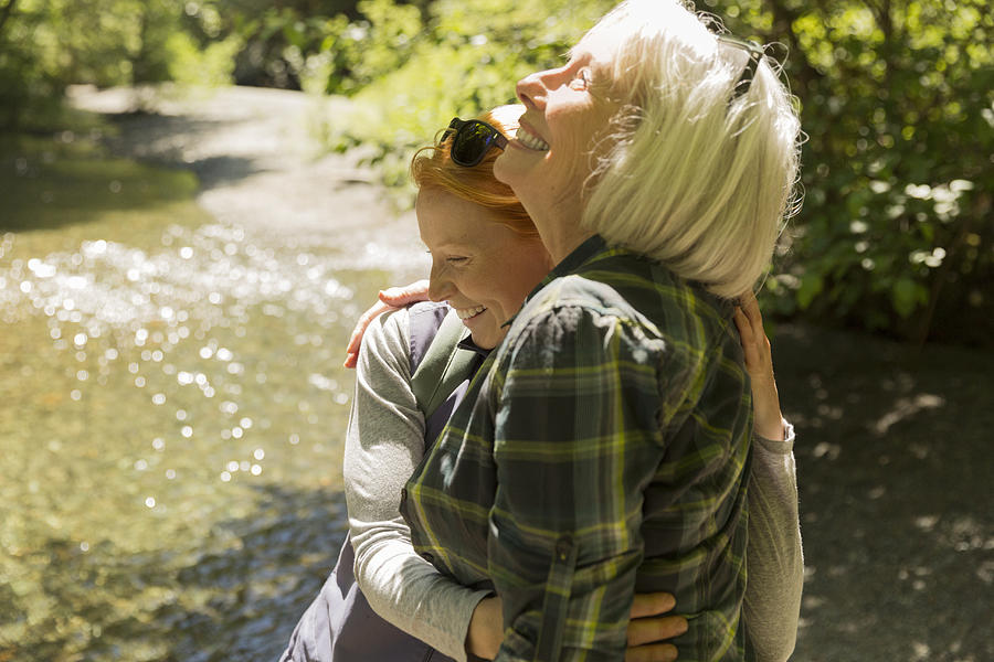 Senior woman and daughter hiking hugging by river Photograph by Compassionate Eye Foundation/Steven Errico