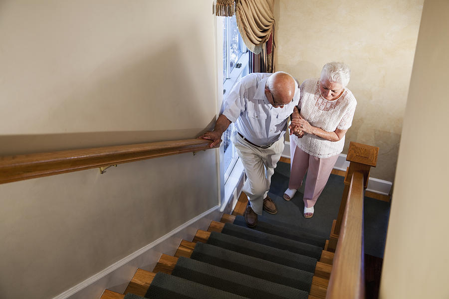 Senior woman helping husband climb staircase Photograph by Kali9