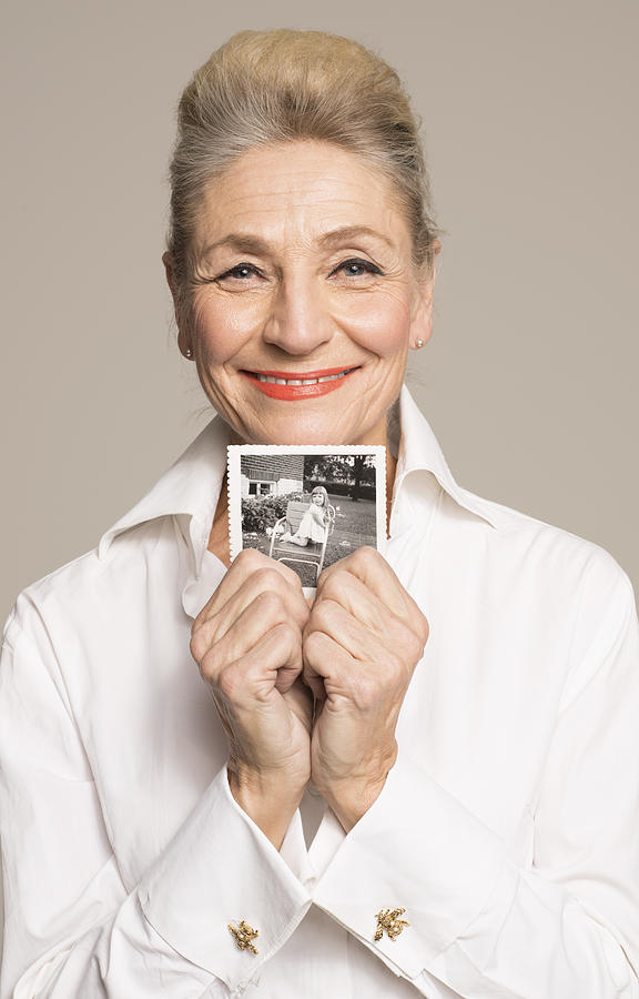 Senior woman holding photo of her younger self Photograph by Compassionate Eye Foundation