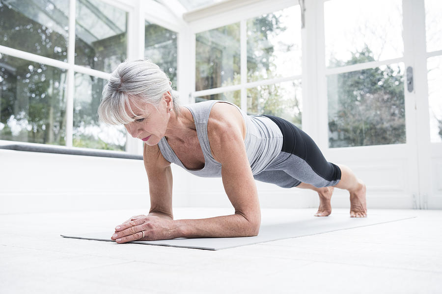 Senior woman in plank position in conservatory Photograph by JohnnyGreig