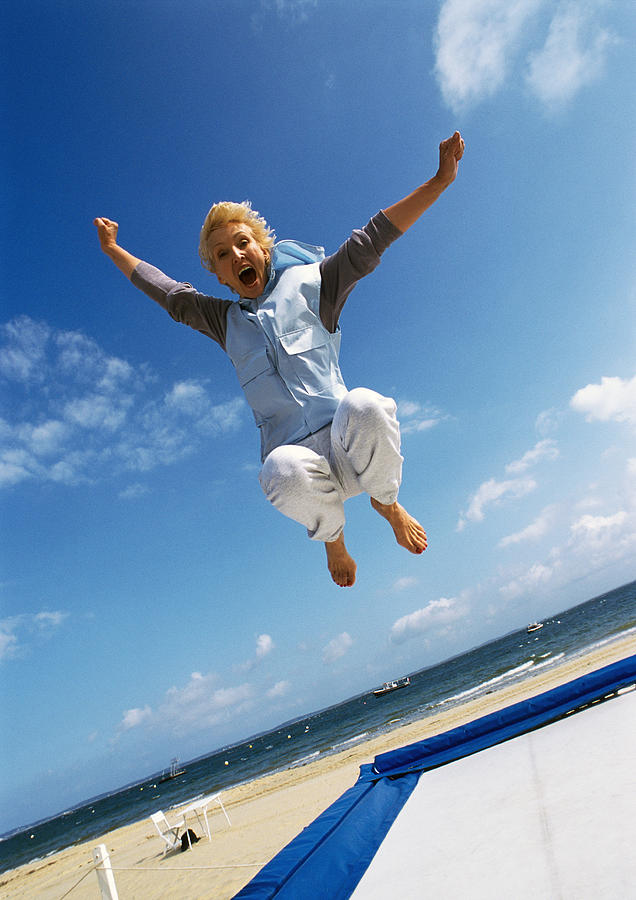 Senior woman jumping on trampoline at beach. Photograph by Teo Lannie
