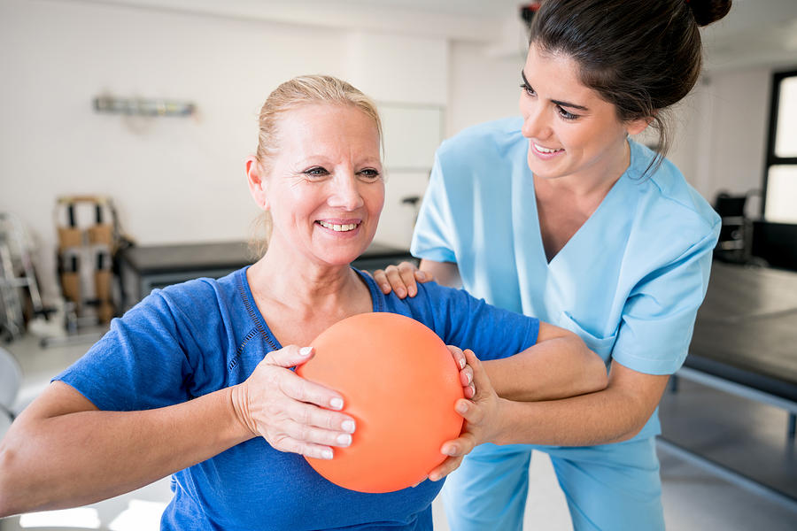 Senior woman patient at physical recovery therapy exercising with a ball and therapist helping her Photograph by Andresr