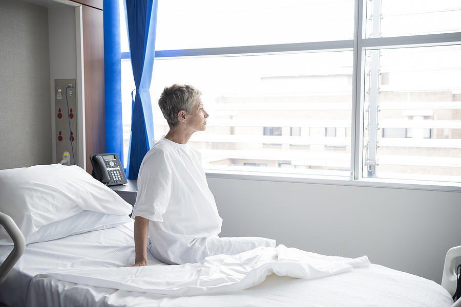 Senior woman sitting on hospital bed looking out of window Photograph by JohnnyGreig