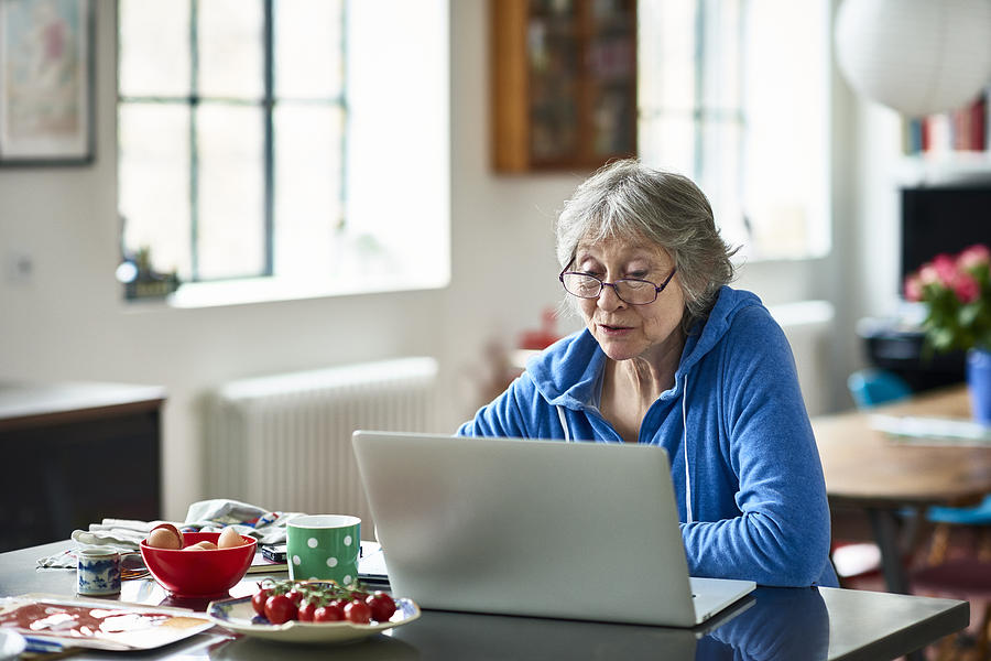 Senior woman wearing glasses using laptop at home Photograph by 10000 Hours