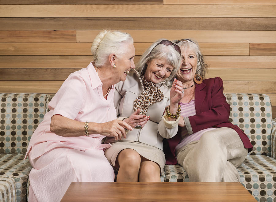 Senior women friends laughing on sofa Photograph by Colin Hawkins