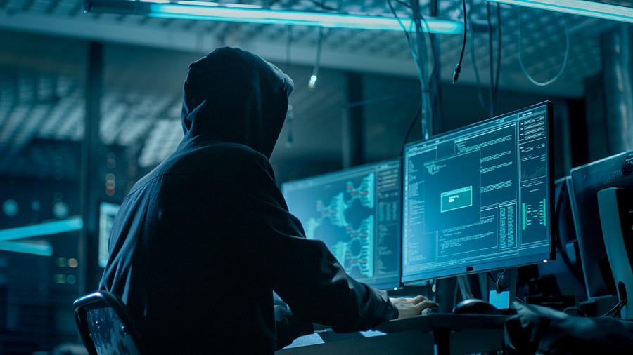 Shot from the Back to Hooded Hacker Breaking into Corporate Data Servers from His Underground Hideout. Place Has Dark Atmosphere, Multiple Displays, Cables Everywhere. Photograph by Gorodenkoff
