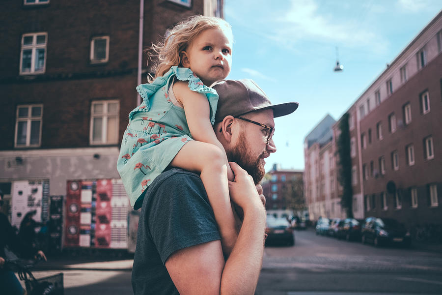 Side view of father carrying daughter on shoulders at city street Photograph by Maskot