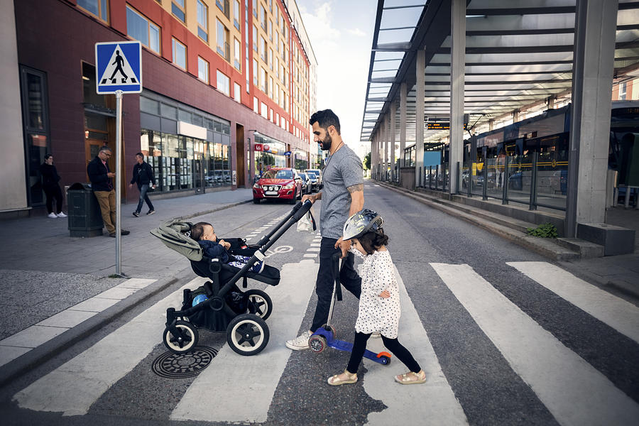 Side view of father crossing street with daughter while holding baby stroller in city Photograph by Maskot