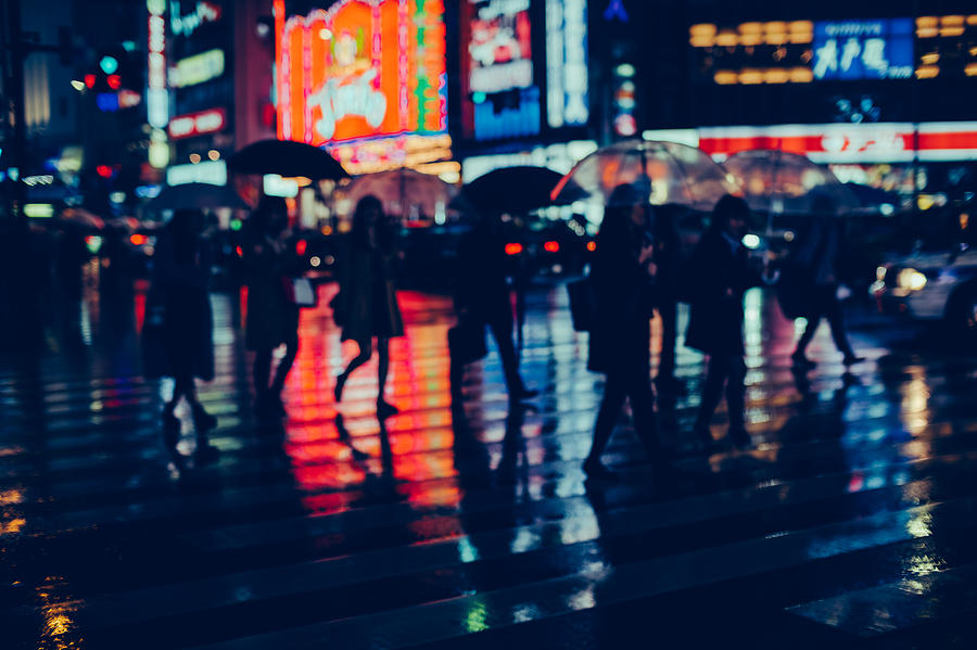 Silhouette of pedestrians crossing street against glowing neon lights in the city on a rainy night. Photograph by D3sign